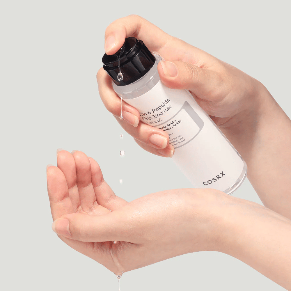 Mani che versano un prodotto per la cura della pelle da una bottiglia trasparente con il testo "The Peptide Skin Booster".