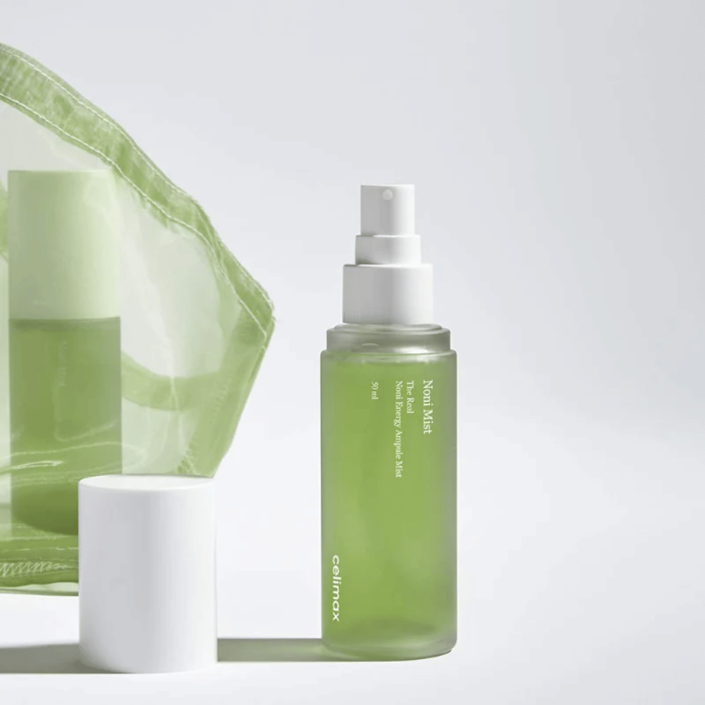 Una bottiglia di Celimax Noni Mist, uno spruzzatore verde con pompa bianca, che si trova accanto a un tappo. Il prodotto è confezionato in una busta di plastica trasparente ed è commercializzato come Noni Energy Ampule Mist.