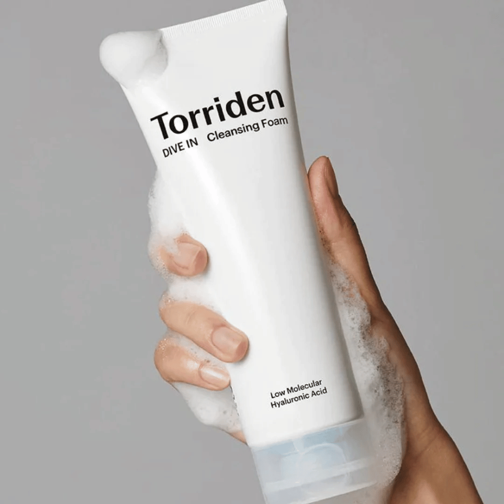 Una mano che tiene un tubo pH-bilanciato Torriden DIVE-IN Low Molecular Hyaluronic Acid Cleansing Foam 150ml.