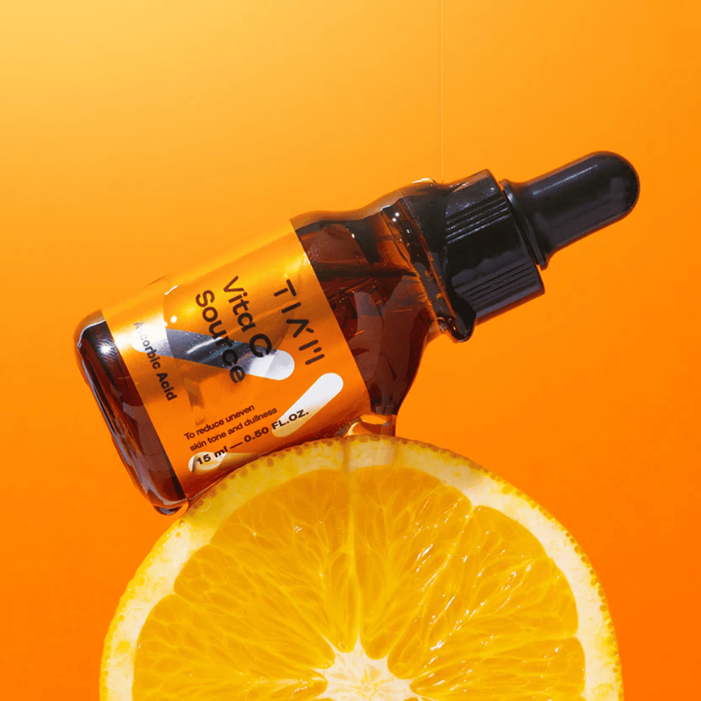 TIA'M Vita C Source-bottiglia posizionata contro un'arancia e uno sfondo arancione che simboleggia la freschezza della vitamina C e il suo effetto antiossidante.