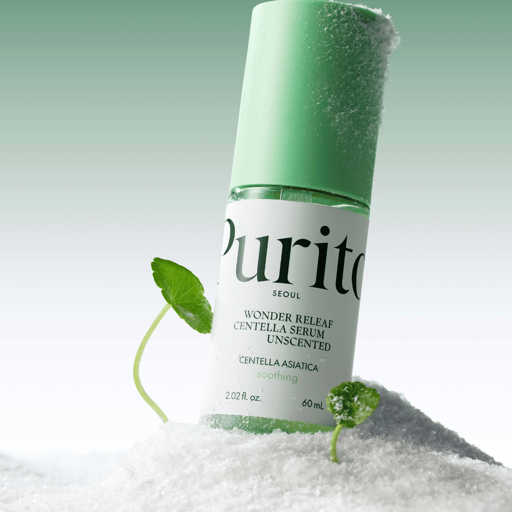 Bottiglia con Purito Centella Serum giace nella neve, si vedono foglie verdi, su uno sfondo verde morbido.