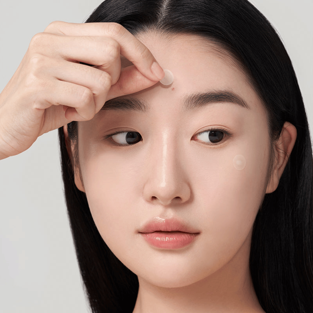 Persona applica Purito Wonder Releaf Centella Spot Patch su un brufolo sulla fronte, un cerotto per acne discreto che protegge, lenisce e supporta la guarigione della pelle.
