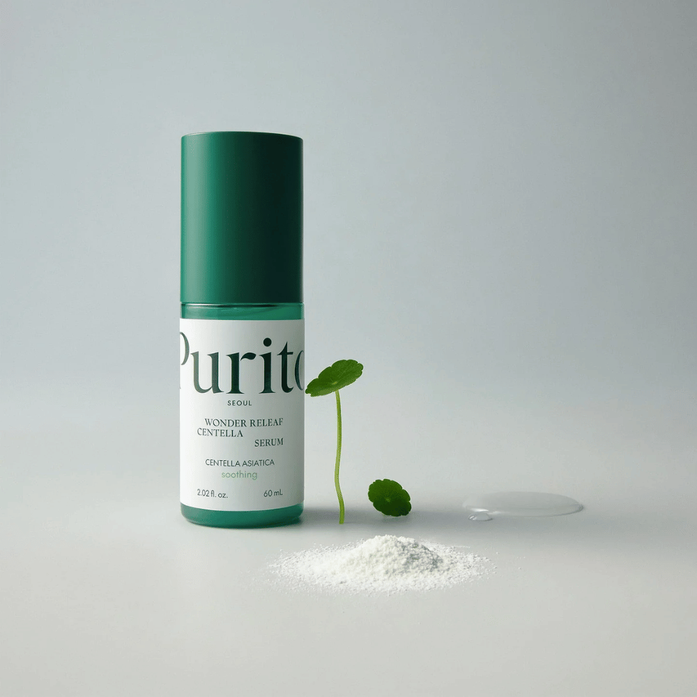 Bottiglia verde di Purito Wonder Releaf Centella Serum 60 ml posizionata su una base bianca, circondata da foglie di centella, una goccia di siero trasparente e una piccola polvere bianca.