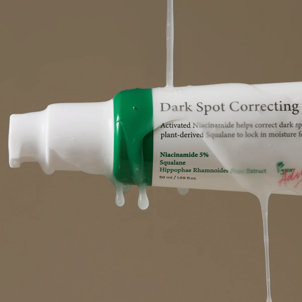 Primo piano di un flacone con pompa di Axis-Y Dark Spot Correcting Glow Serum con confezione bianca e tappo verde, coperto da liquido trasparente che scorre.