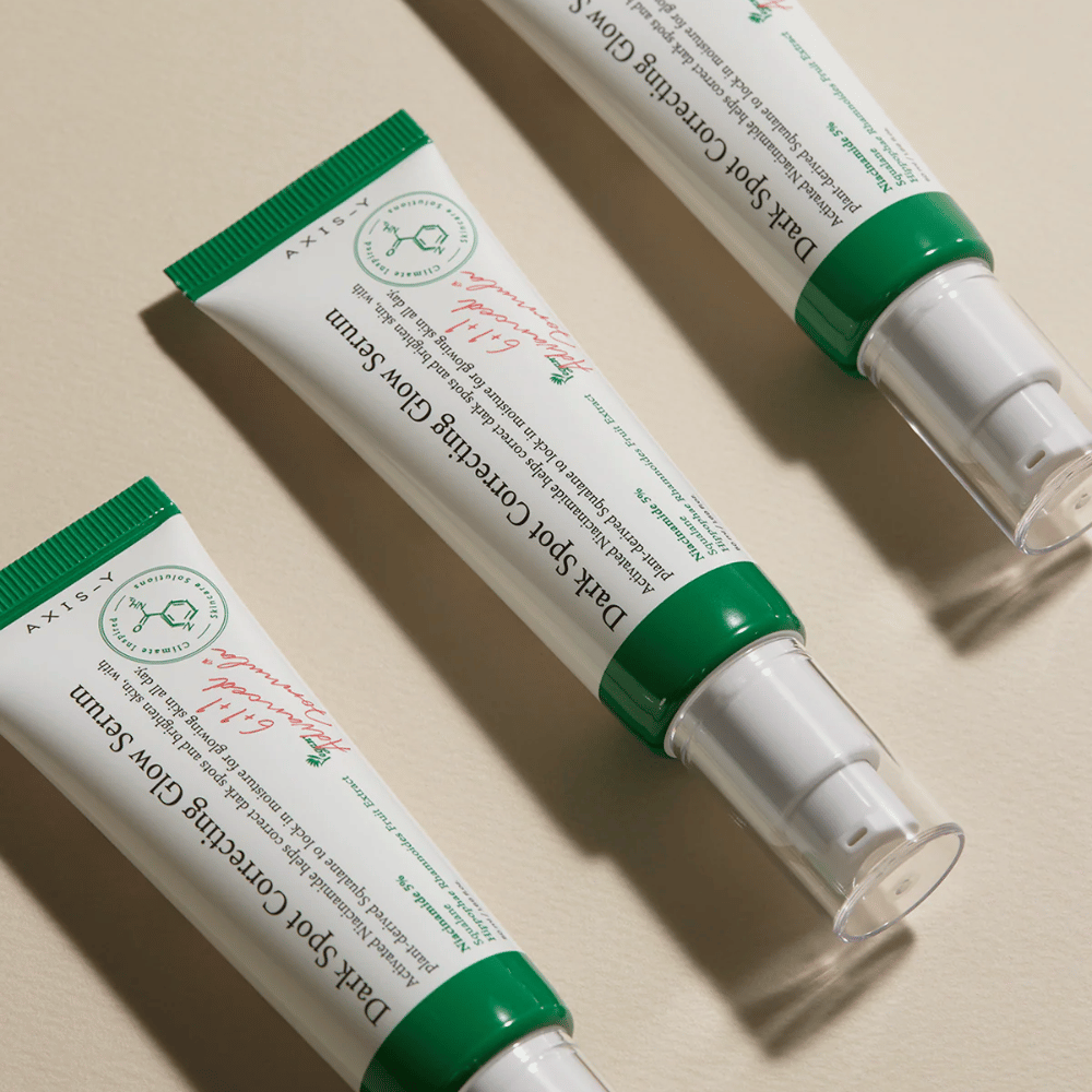 Tre tubi di Axis-Y Dark Spot Correcting Glow Serum con tappo verde e confezione bianca su una superficie chiara.