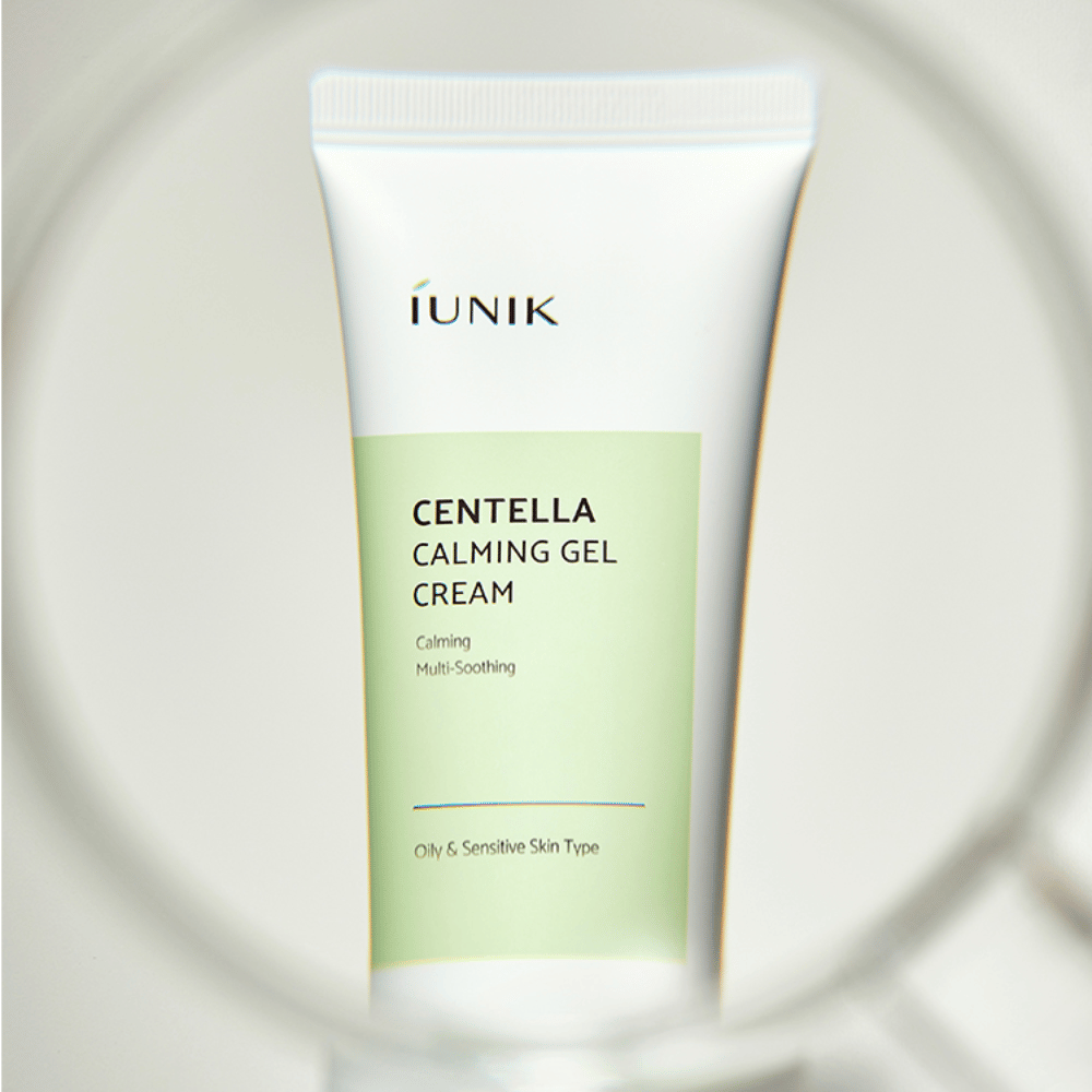 Un tubo iUNIK Centella Calming Gel Cream con design bianco e verde chiaro è in piedi, visto attraverso una cornice rotonda simile a una lente d'ingrandimento.