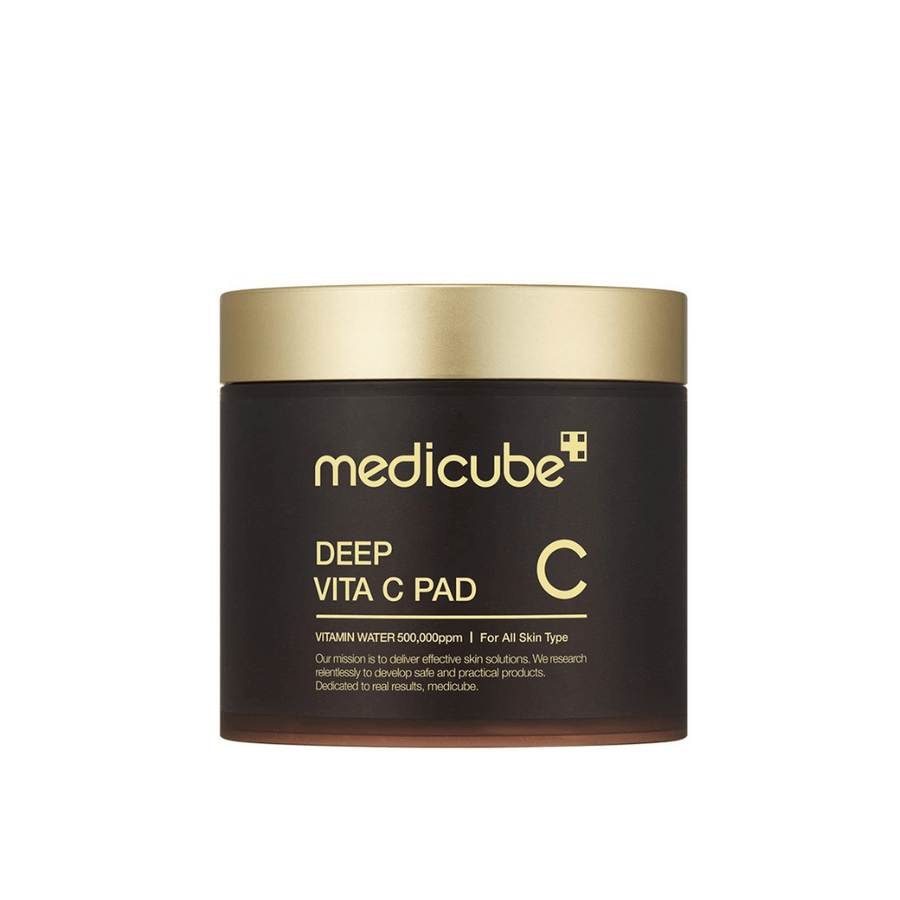 En burk från medicube, märkt "Deep Vita C Pad", med guldlock och mörk kropp. Text på burken anger C-vitamin och lämplighet för alla hudtyper. Bakgrunden är neutral.