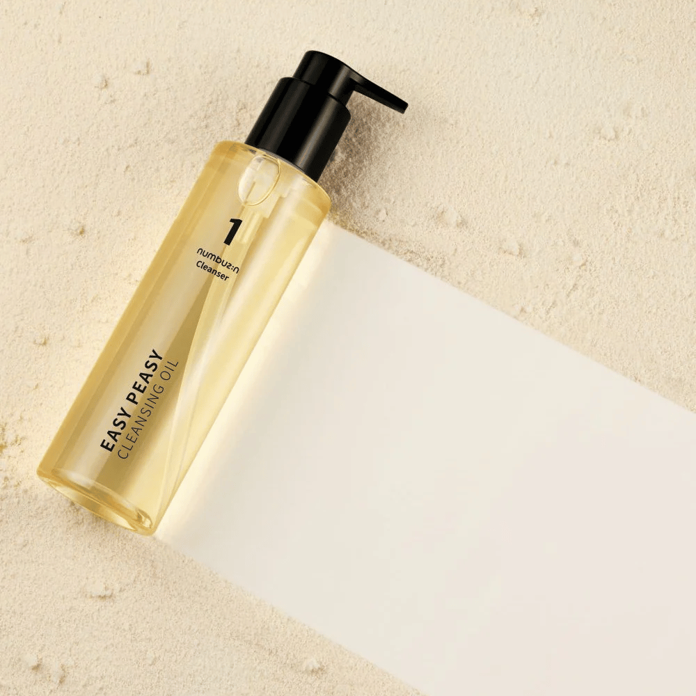 Numbuzin No.1 Easy Peasy Cleansing Oil adagiato su una superficie color sabbia con ombra.