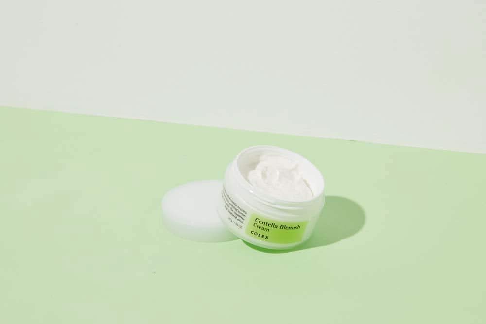 Un barattolo di COSRX Centella Blemish Cream 30ml che si trova su una superficie verde.