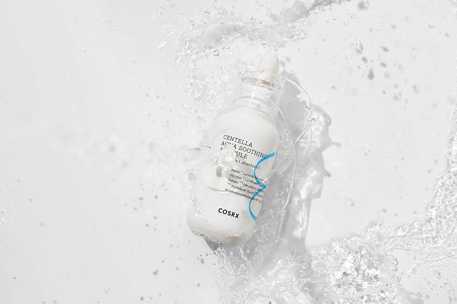 Una bottiglia COSRX Centella Aqua Soothing Ampoule 40ml che spruzza su una superficie bianca, riduce il rossore e fornisce idratazione calmante.
