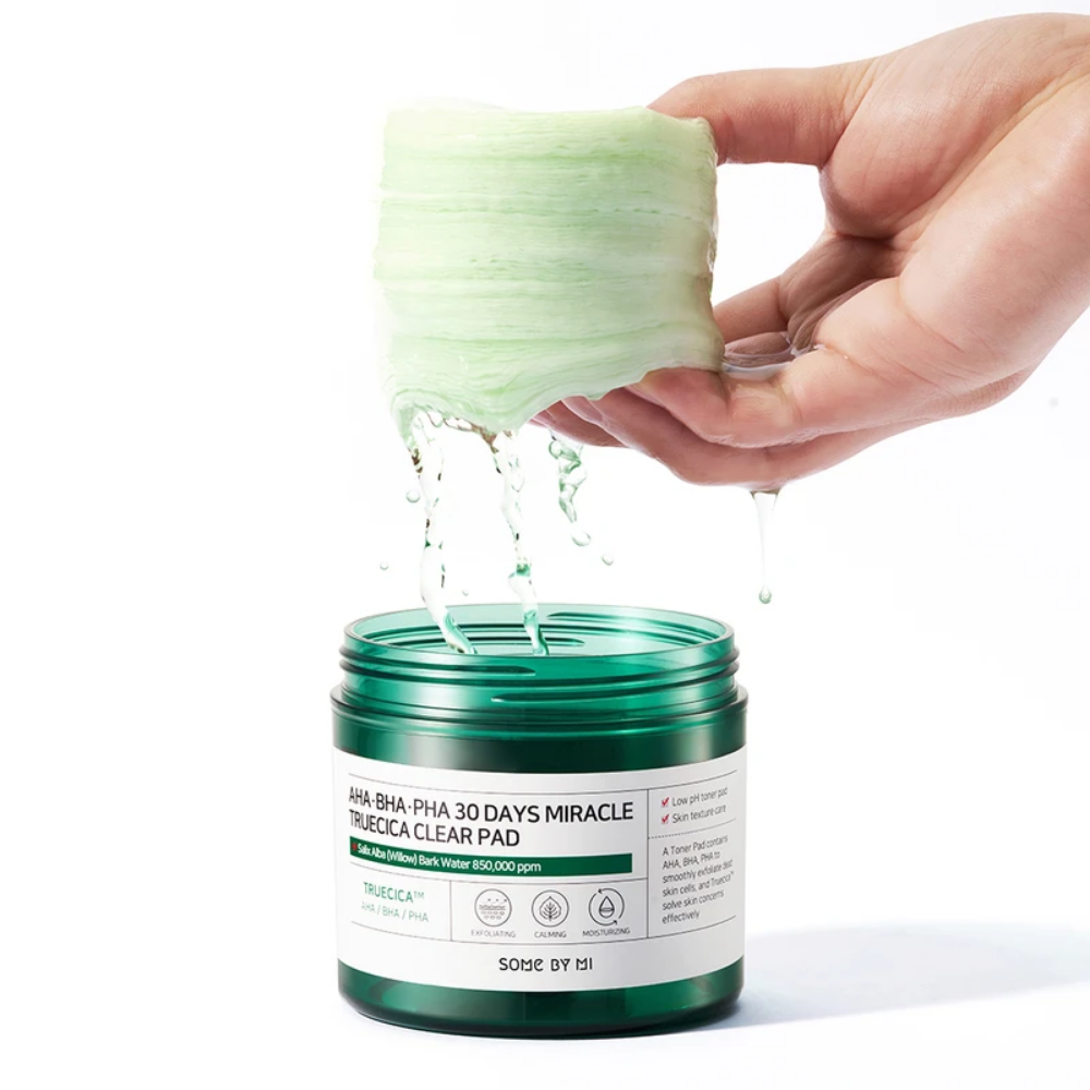 Una mano versa un liquido verde in un barattolo per il trattamento degli sfoghi di acne di SOME BY MI:s AHA, BHA, PHA 30 Days Miracle Truecica Clear Pad 70 pezzi.