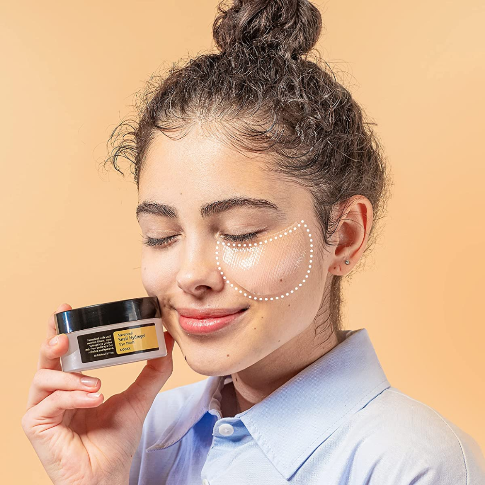 Una donna che tiene in mano un barattolo COSRX Advanced Snail Hydrogel Eye Patch 60 pz crema per il viso.