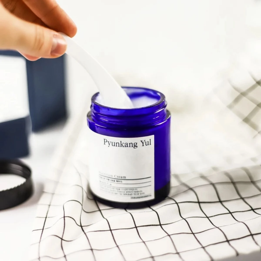 Una persona usa un barattolo Pyunkang Yul Nutrition Cream 100ml su un tavolo.