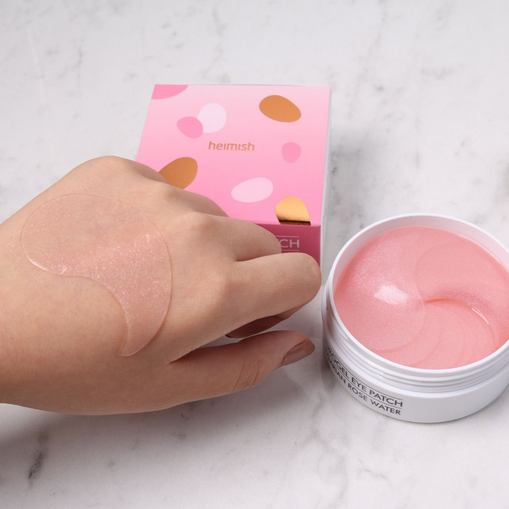 Una mano che tiene un rosa Bulgarian Rose Hydrogel Eye Patch 60st da heimish e applica una maschera per occhi.