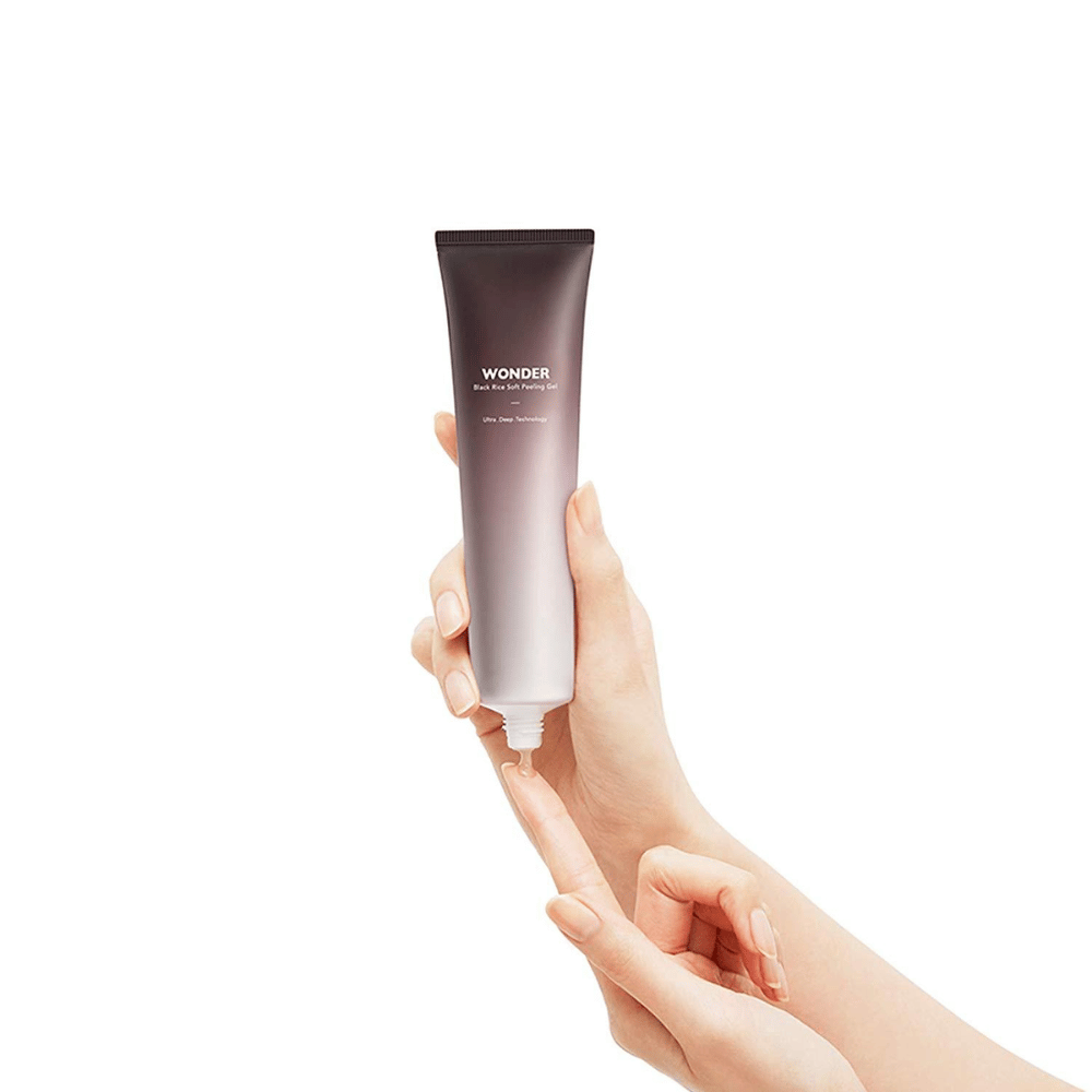 La mano di una donna che tiene un tubo Haruhuru Wonders Black Rice Soft Peeling Gel 100 ml su uno sfondo bianco.