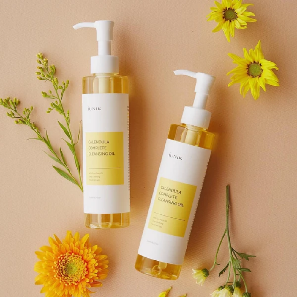 Due bottiglie iUNIK Calendula Complete Cleansing Oil 200ml con fiori gialli su sfondo beige, infuse con olio vegetale.