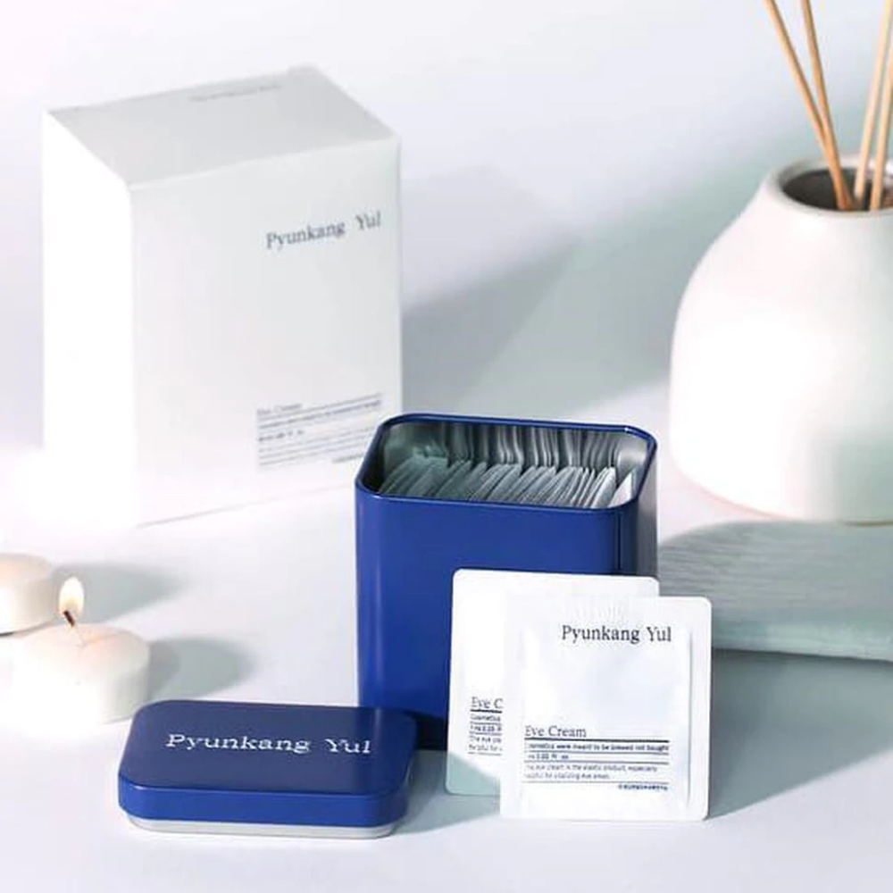 Una scatola bianca con coperchio blu e Pyunkang Yul Crema Occhi 1ml x 50pz accanto.