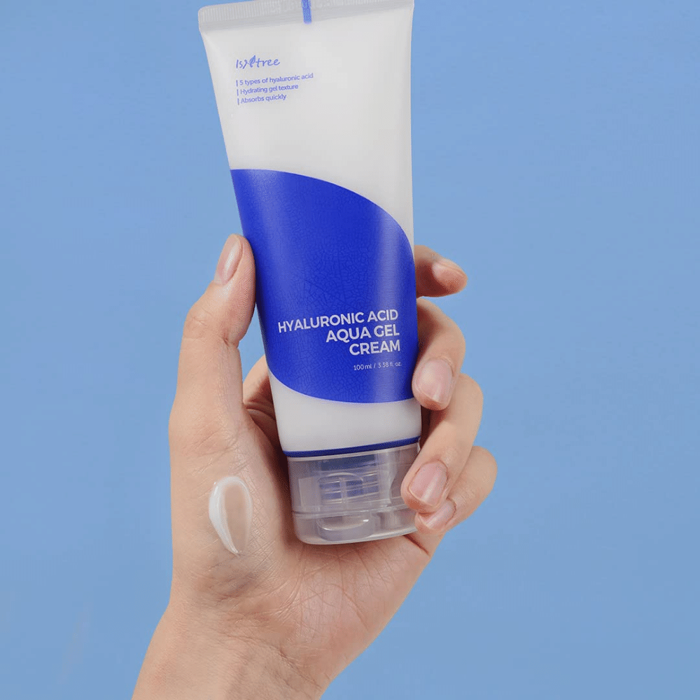 Una mano che tiene un tubo Isntree Hyaluronic Acid Aqua Gel Cream 100ml su uno sfondo blu.