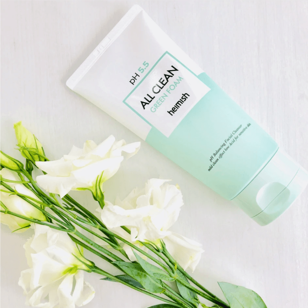 Un tubo heimish All Clean Green Foam 150ml accanto a fiori bianchi.