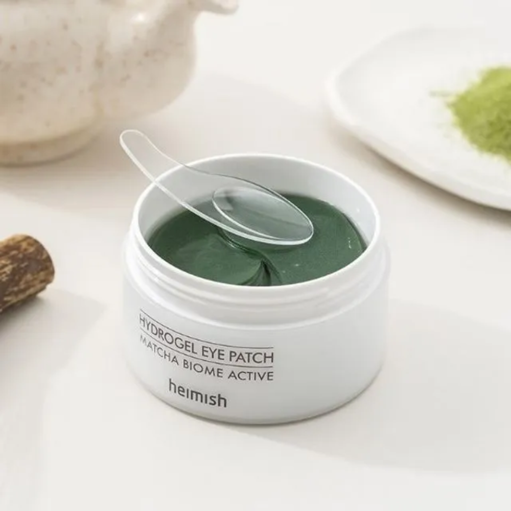 Una ciotola con Heimish Matcha Biome Hydrogel Eye Patch 60 cerotti con un cucchiaio.
